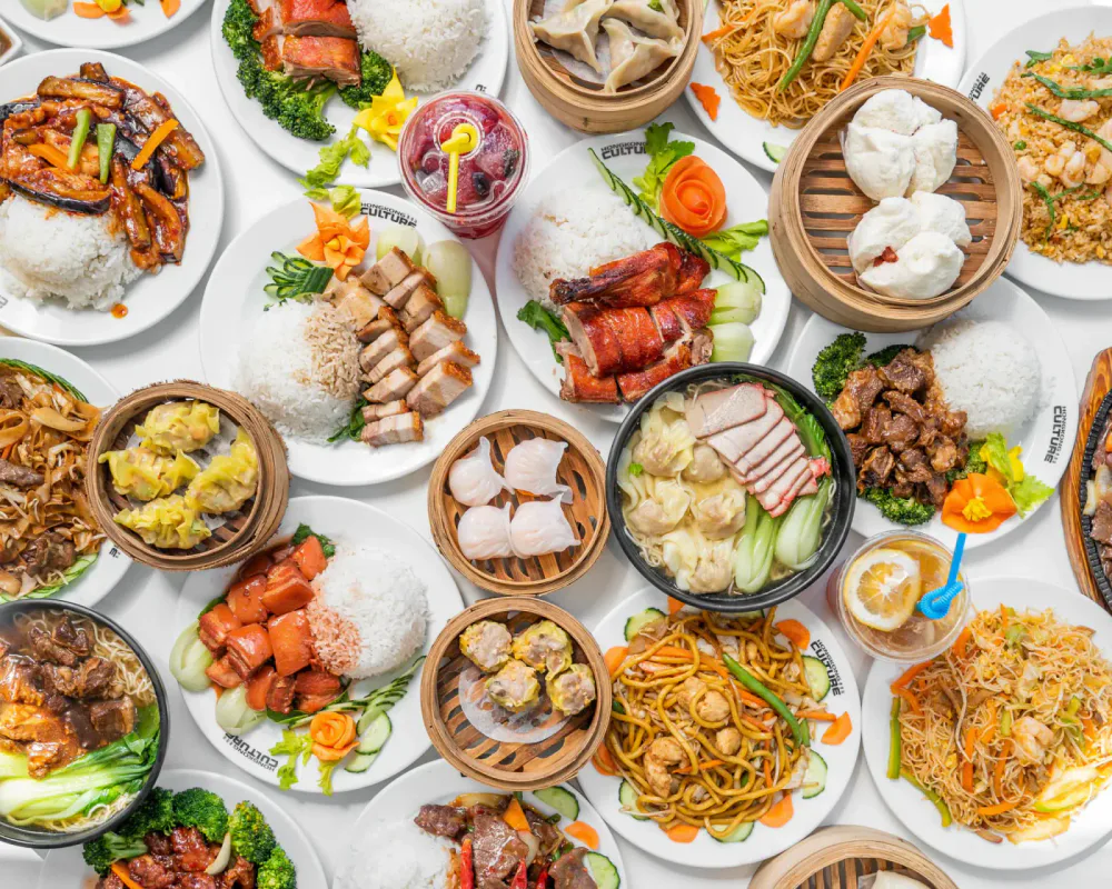 Assorted Asian dishes, including fried rice, noodles, dumplings, steamed buns, and various stir-fries, served on white plates and bamboo steamers.
