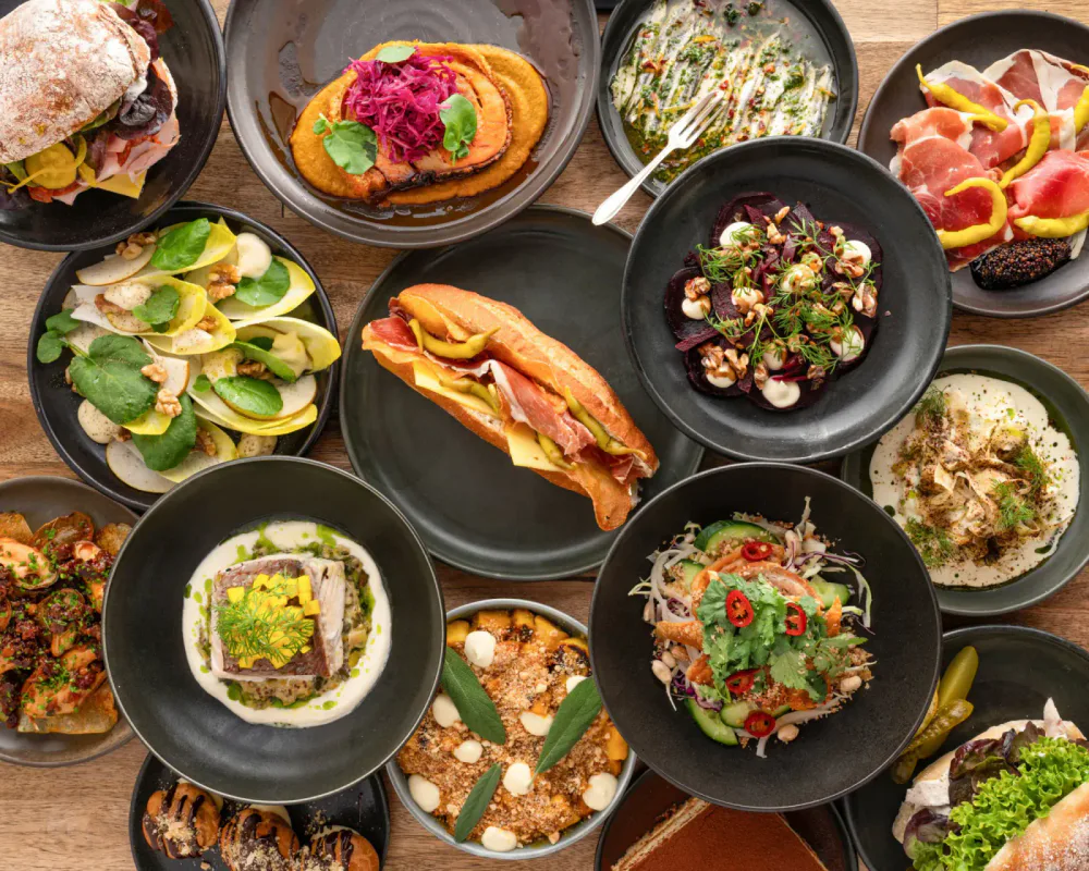 A variety of dishes including sandwiches, salads, and entrees on black plates on a wooden table.