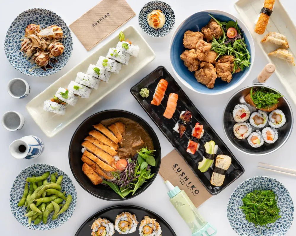 A variety of Japanese sushi dishes arranged on a table, including sushi rolls, sashimi, and accompaniments with soy sauce, wasabi, and edamame.