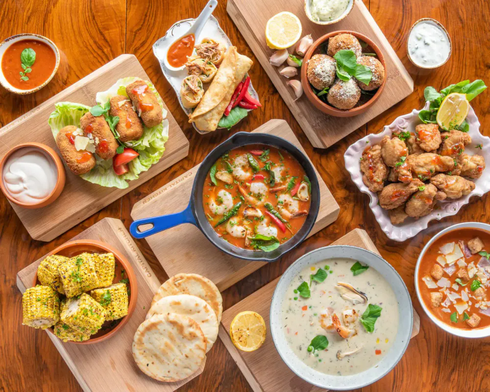 A variety of Indian dishes on wooden platters and bowls, including fried snacks, curries, corn, and naan, served on a wooden table.