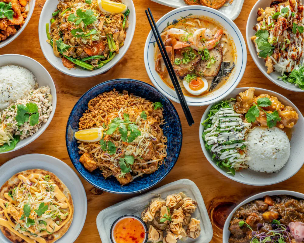 Assortment of Asian dishes including rice, noodles, stir-fry, and dumplings served on a wooden table.