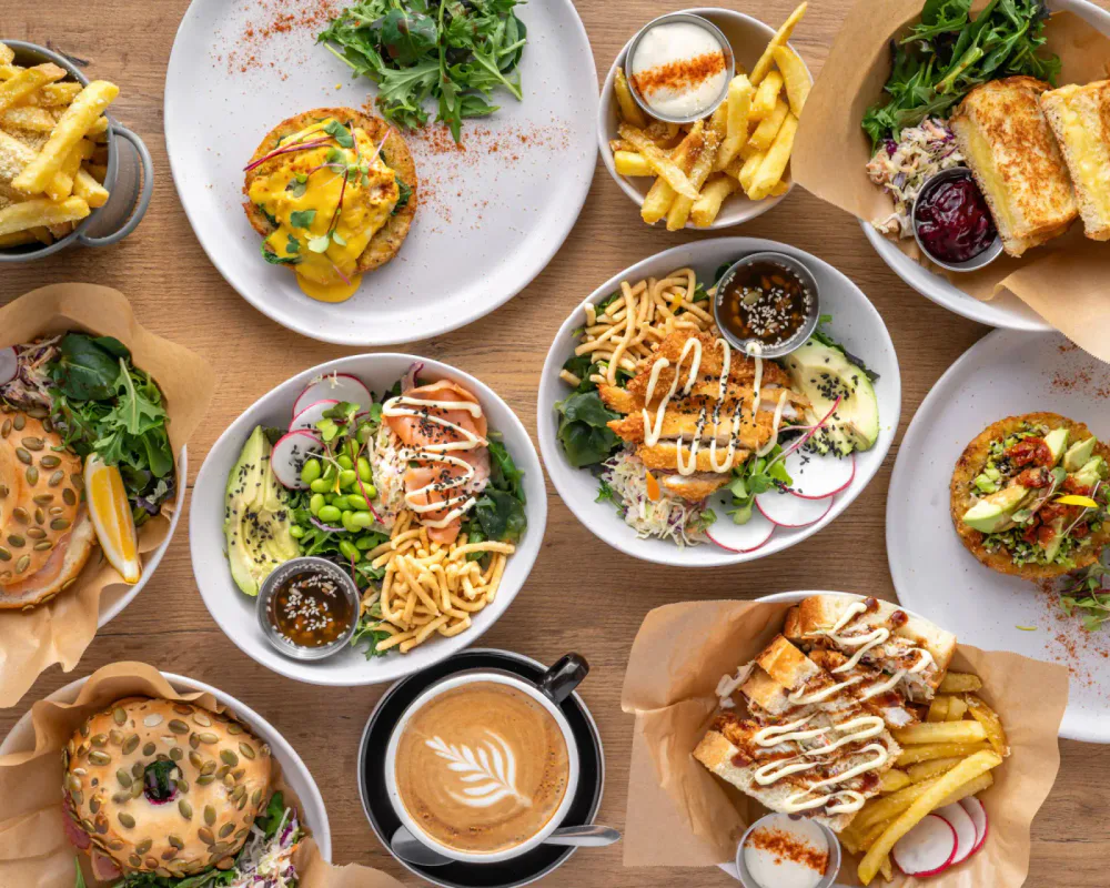 Assorted dishes of salads, sandwiches, fries, and a latte served on a wooden table.