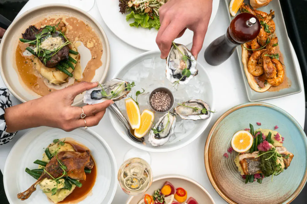 Oysters, seafood, lamb and dessert dishes arranged together on a restaurant table.
