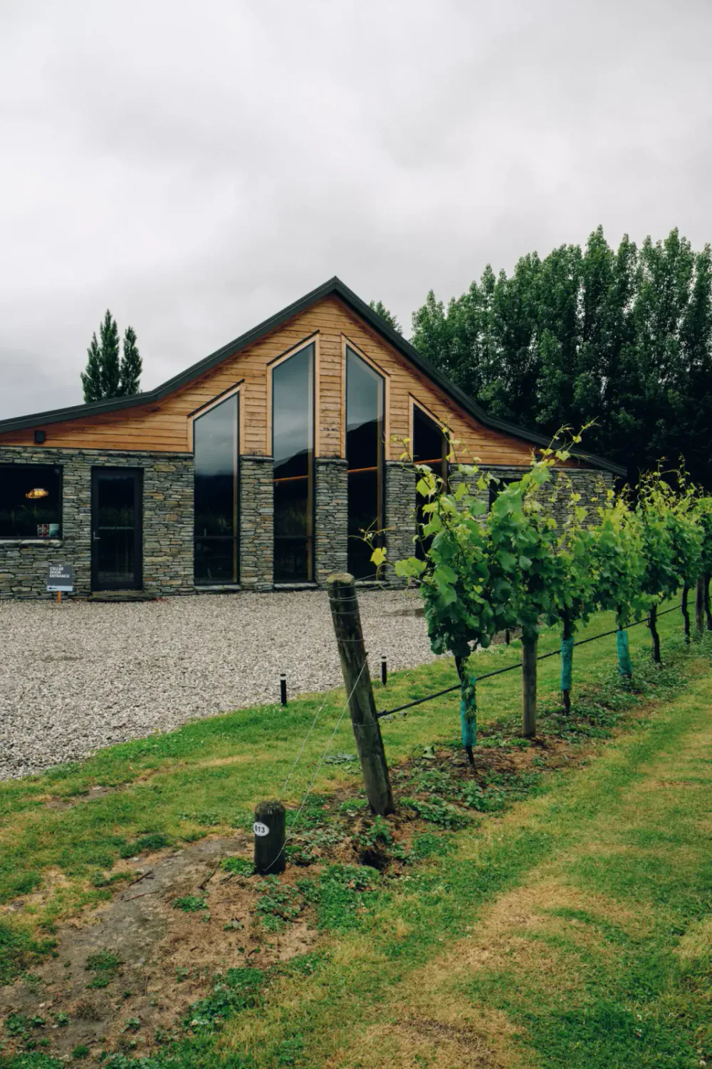 A hospitality venue with tall triangular windows, timber cladding and grapevines around the entrance
