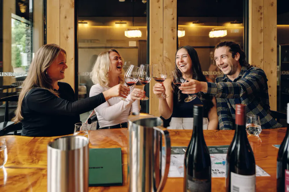 Four friends enjoying a toast with glasses of red wine at a wooden table in a restaurant.
