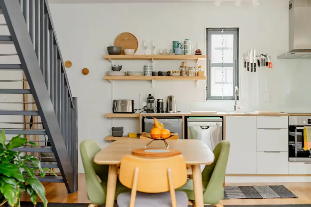 Modern kitchen with open shelving, a dining table with six chairs, and a staircase on the left.