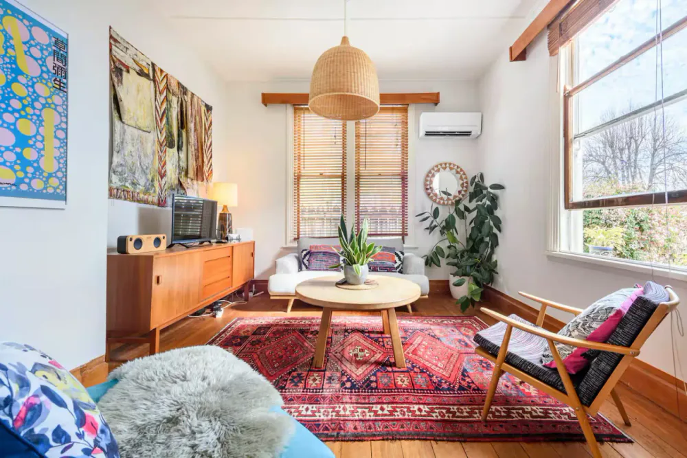 A colourful living room with a white sofa, timber furniture, artwork and a patterned red rug.