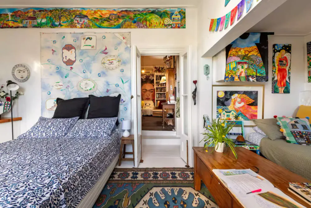 An art-filled bedroom with patterned bedding, black pillows and a view into a mural-lined room.