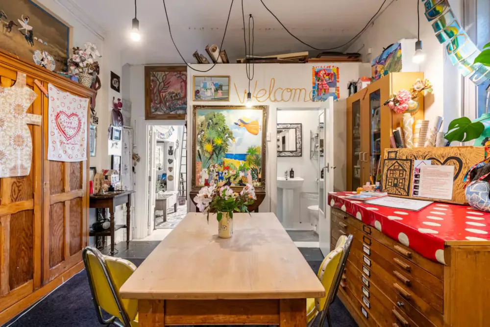 A cozy, eclectic dining room with a wooden table, colorful chairs, and various artwork and decorations on the walls.