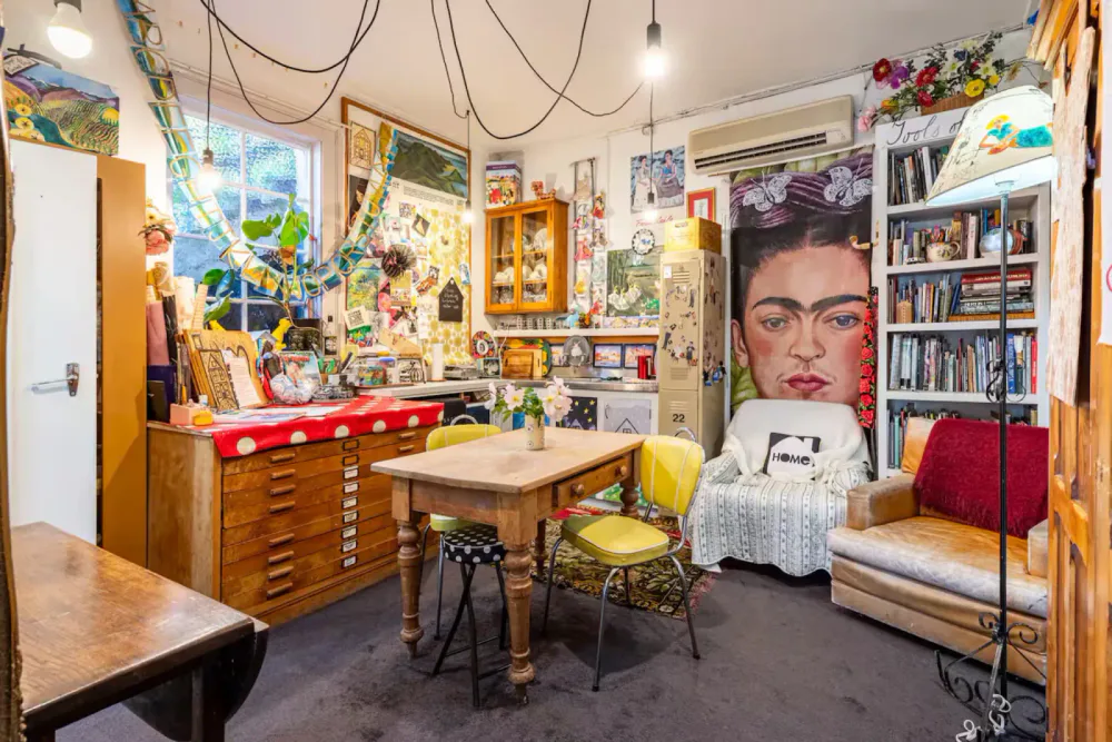 A colourful living space with a Frida Kahlo portrait, yellow dining chairs and a rocking chair.