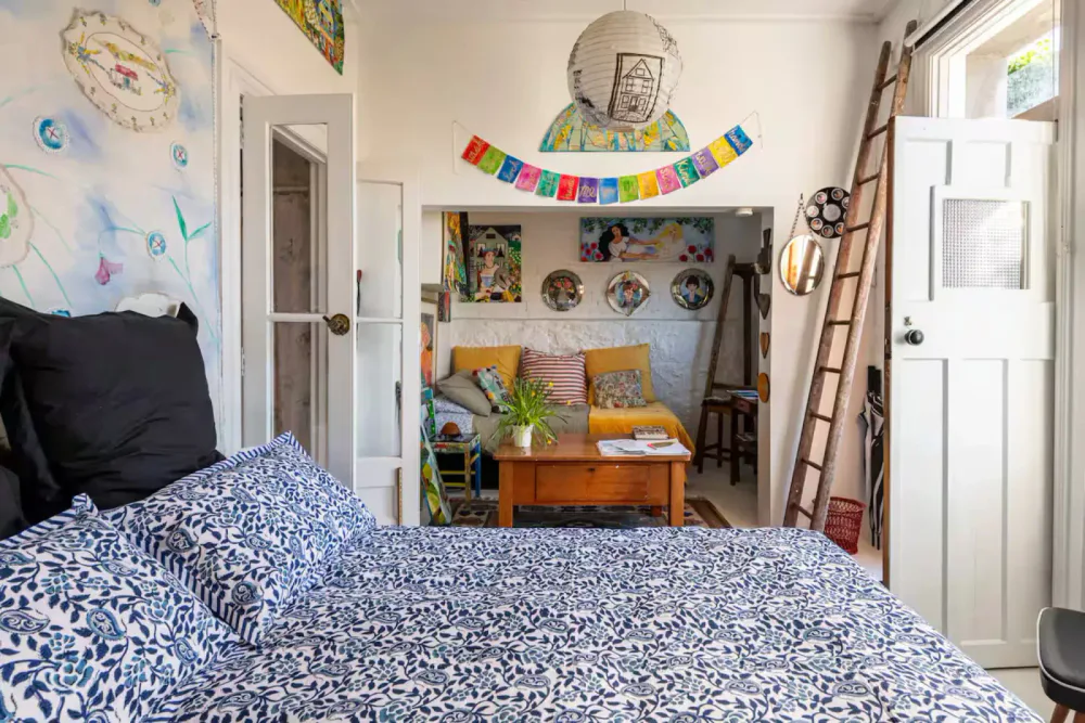 A bright bedroom with blue patterned bedding, black pillows and an artwork-filled seating nook.