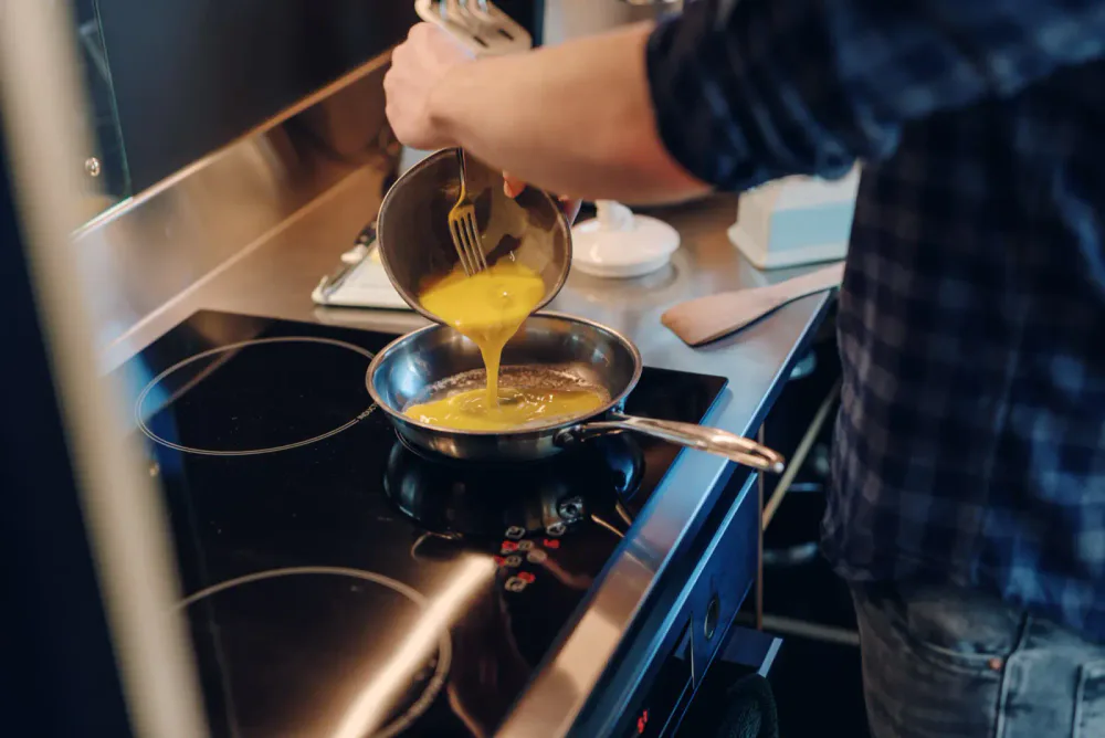 Person pouring beaten eggs from a bowl into a skillet on a stovetop.