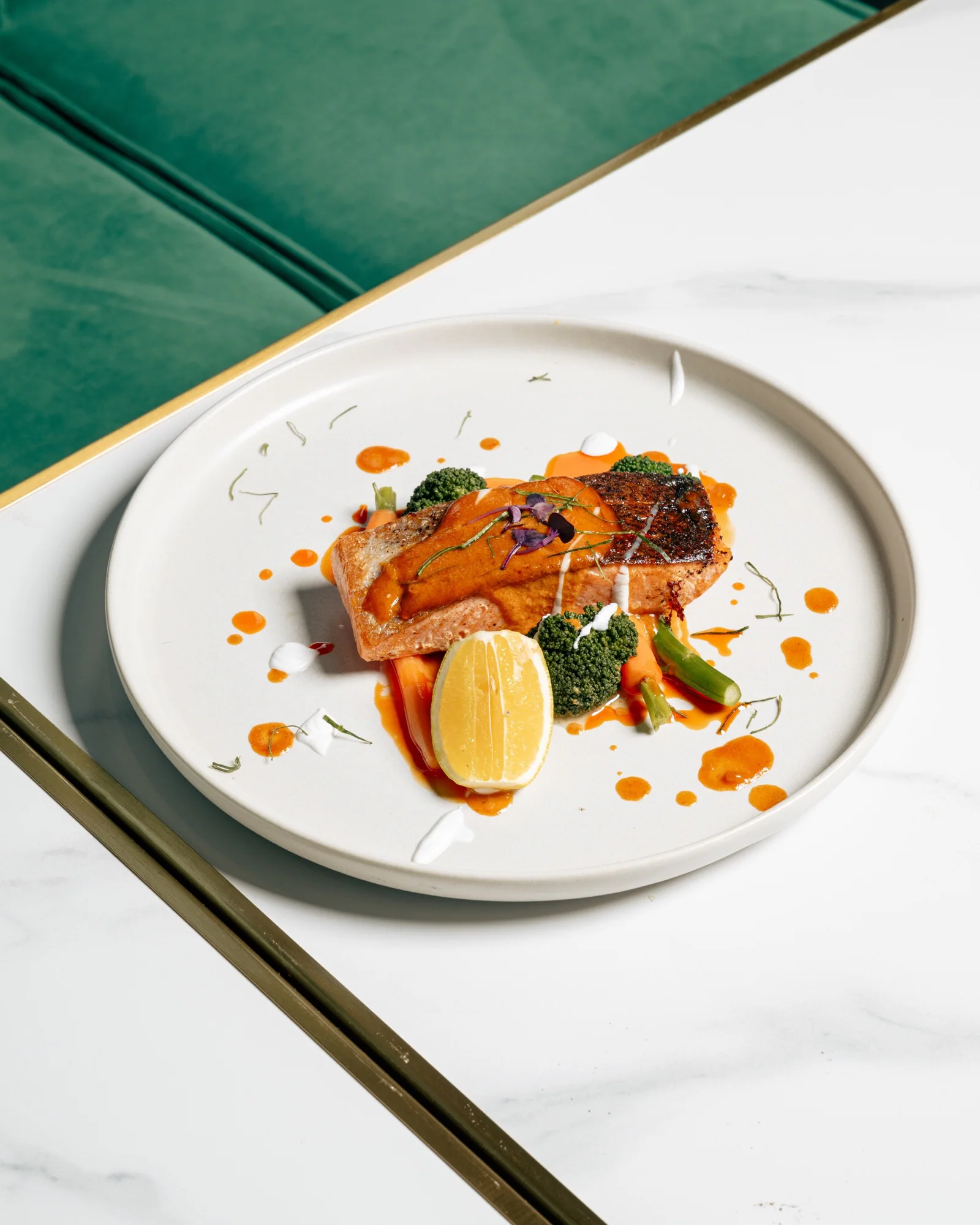 A plated salmon dish with vegetables, lemon and orange sauce on a restaurant table