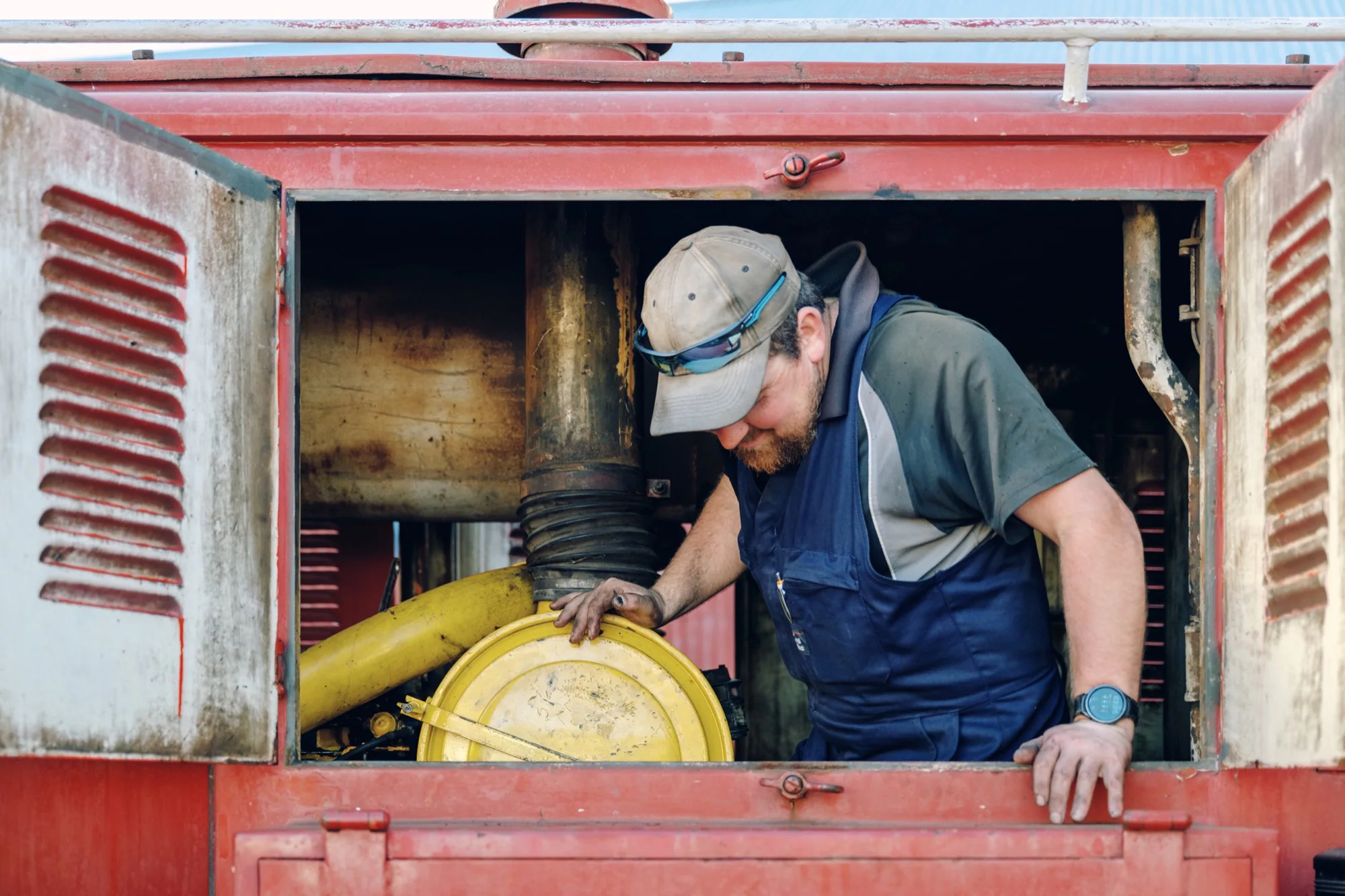 A railway workshop worker servicing machinery inside a red locomotive