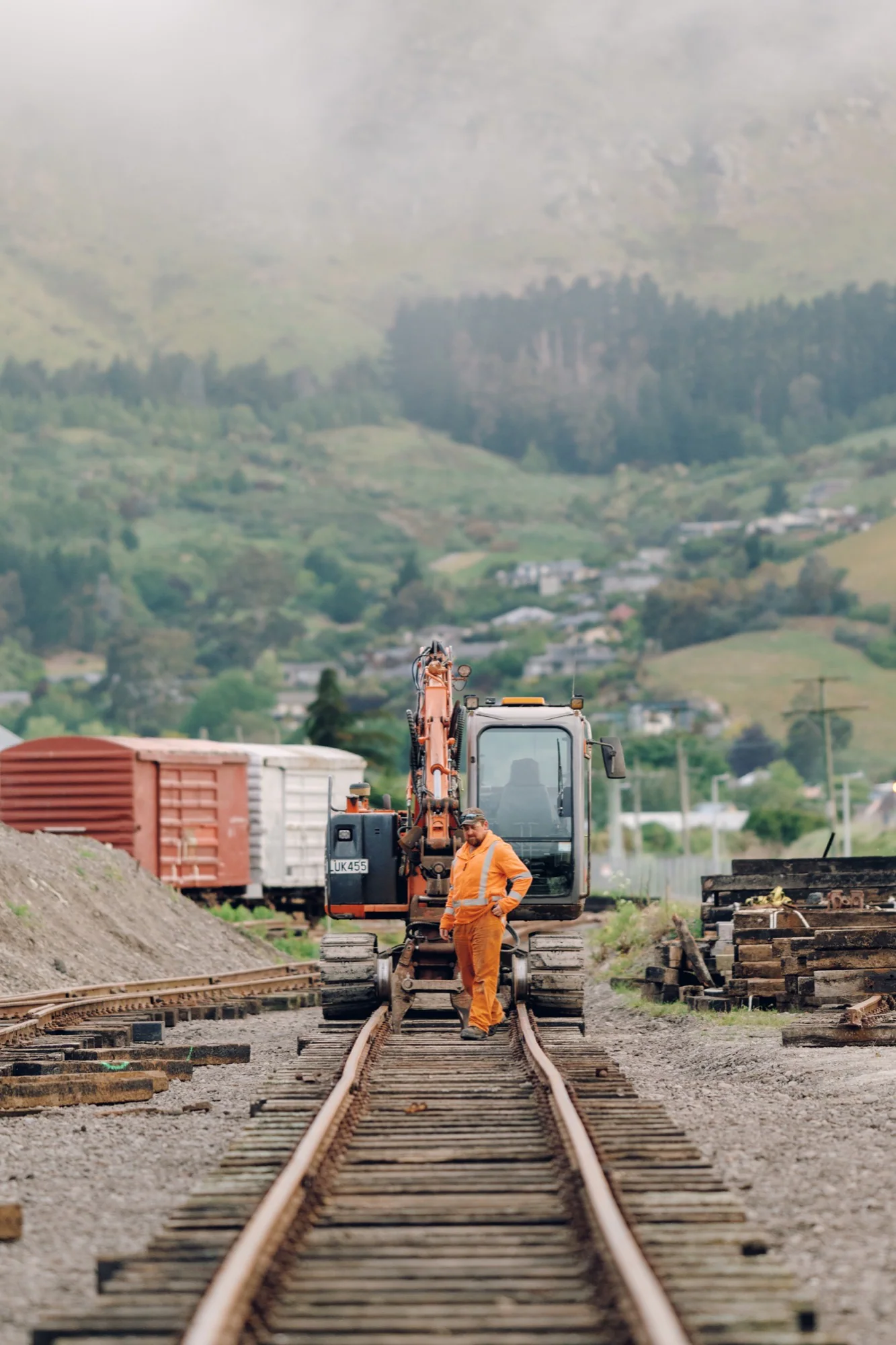 A railway worker standing beside a tracked excavator on rail lines